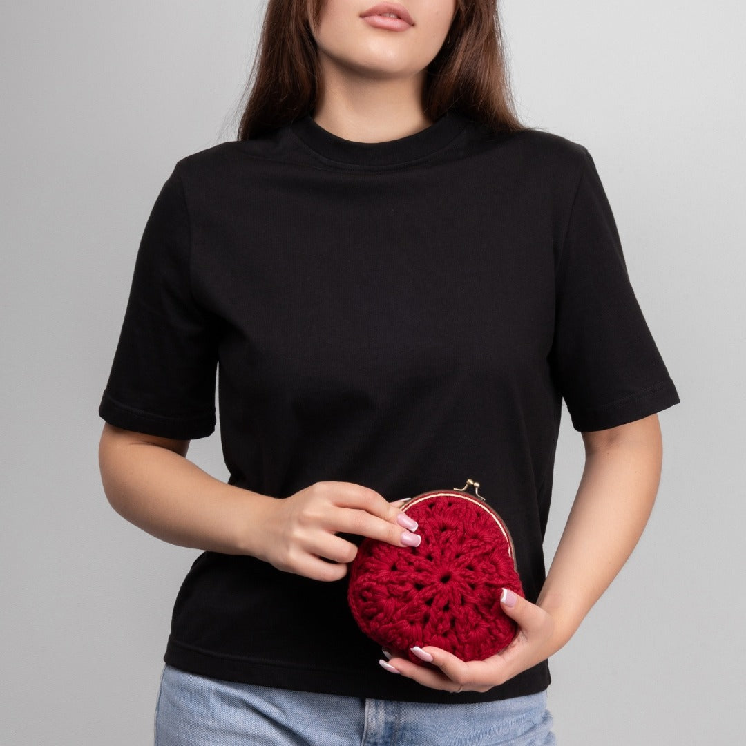 Person holding a red crochet clutch against a gray background
