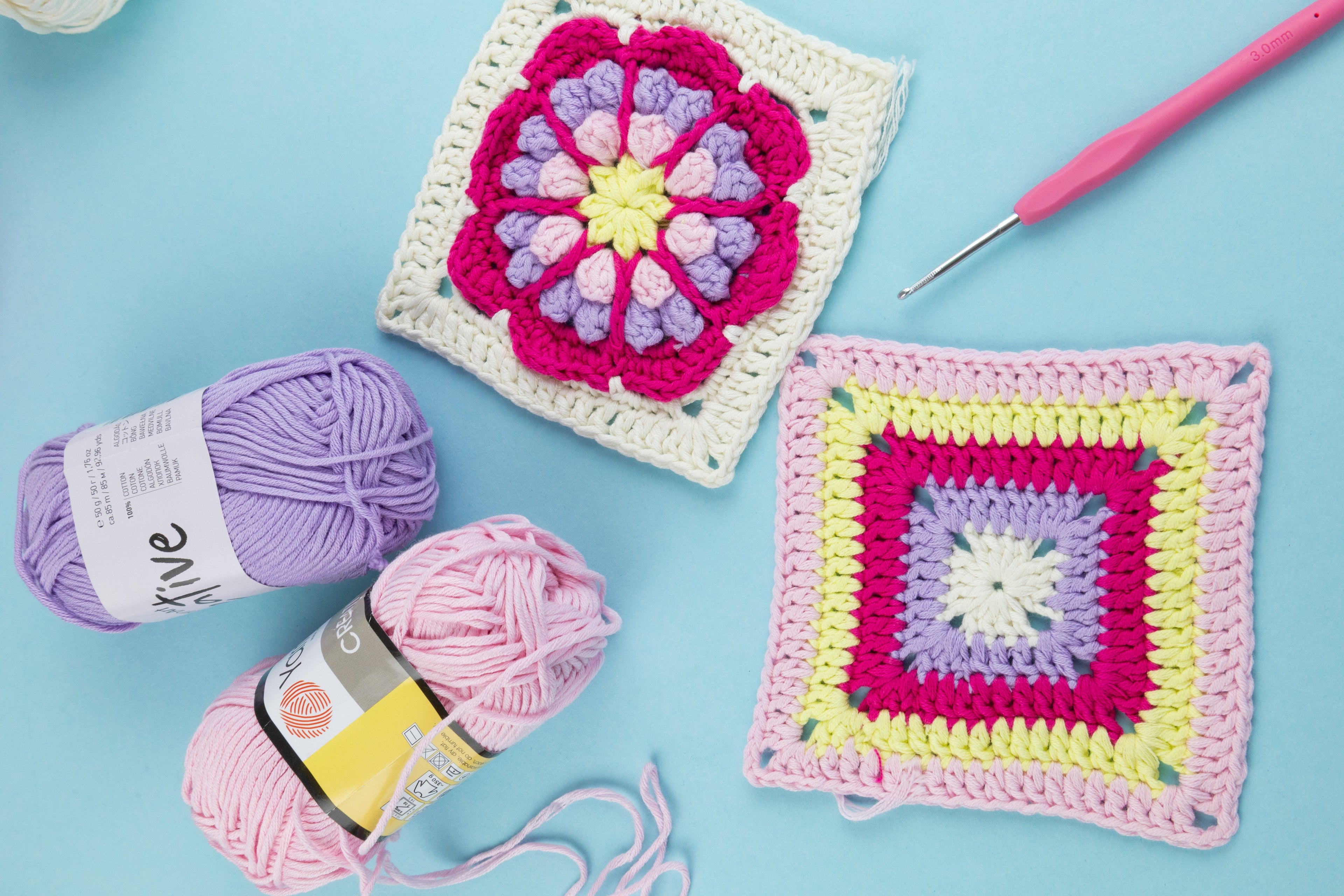 Two colorful crochet squares with yarn and a crochet hook on a blue background