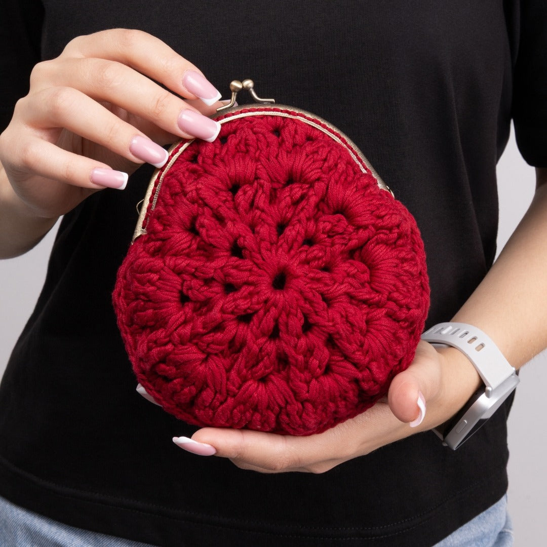 Red crocheted purse held by a person against a black background