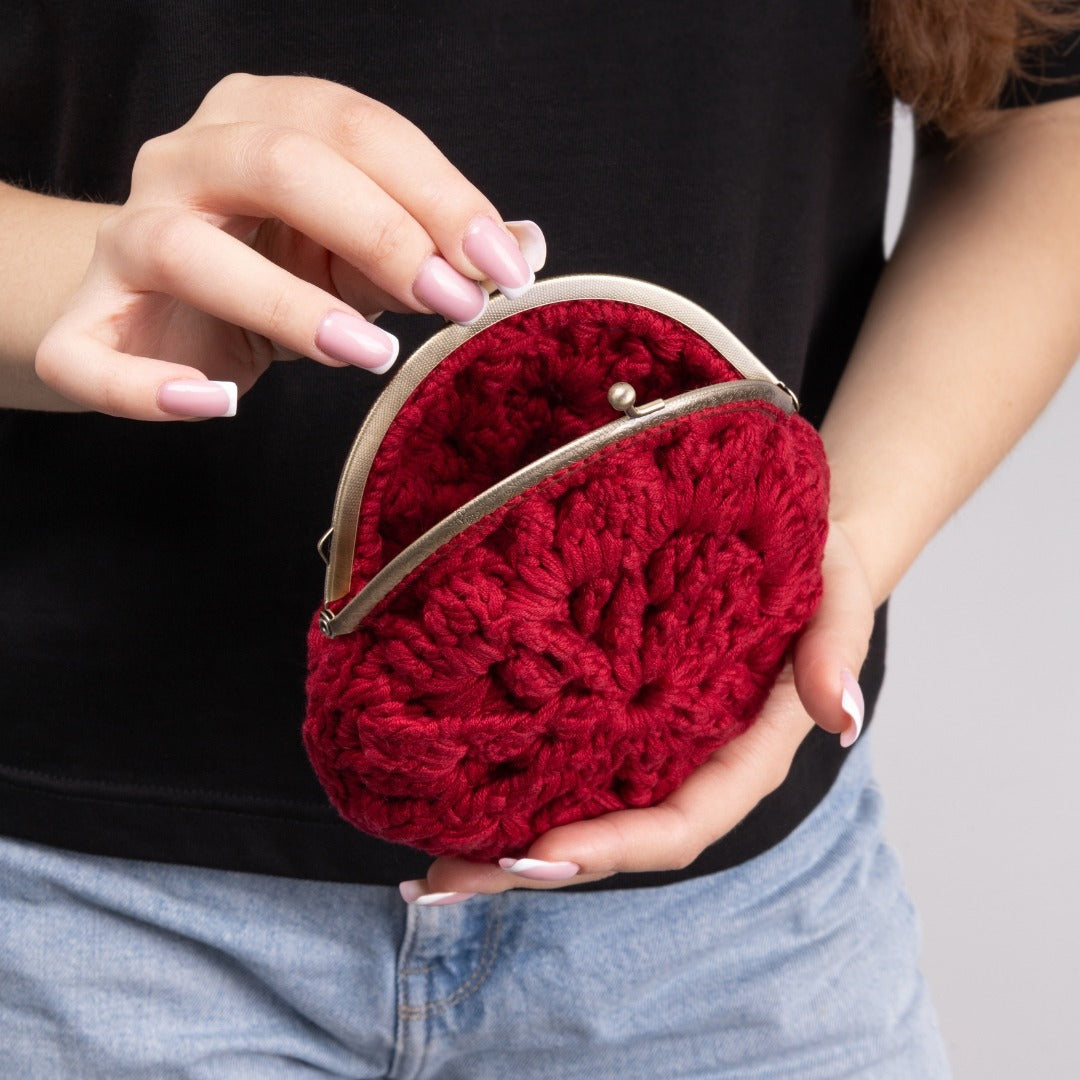 Red crocheted purse held by a person wearing a black shirt and blue jeans.