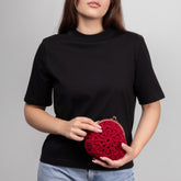 Person holding a red crochet clutch against a gray background