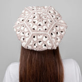 Person wearing a beige crochet hat against a gray background
