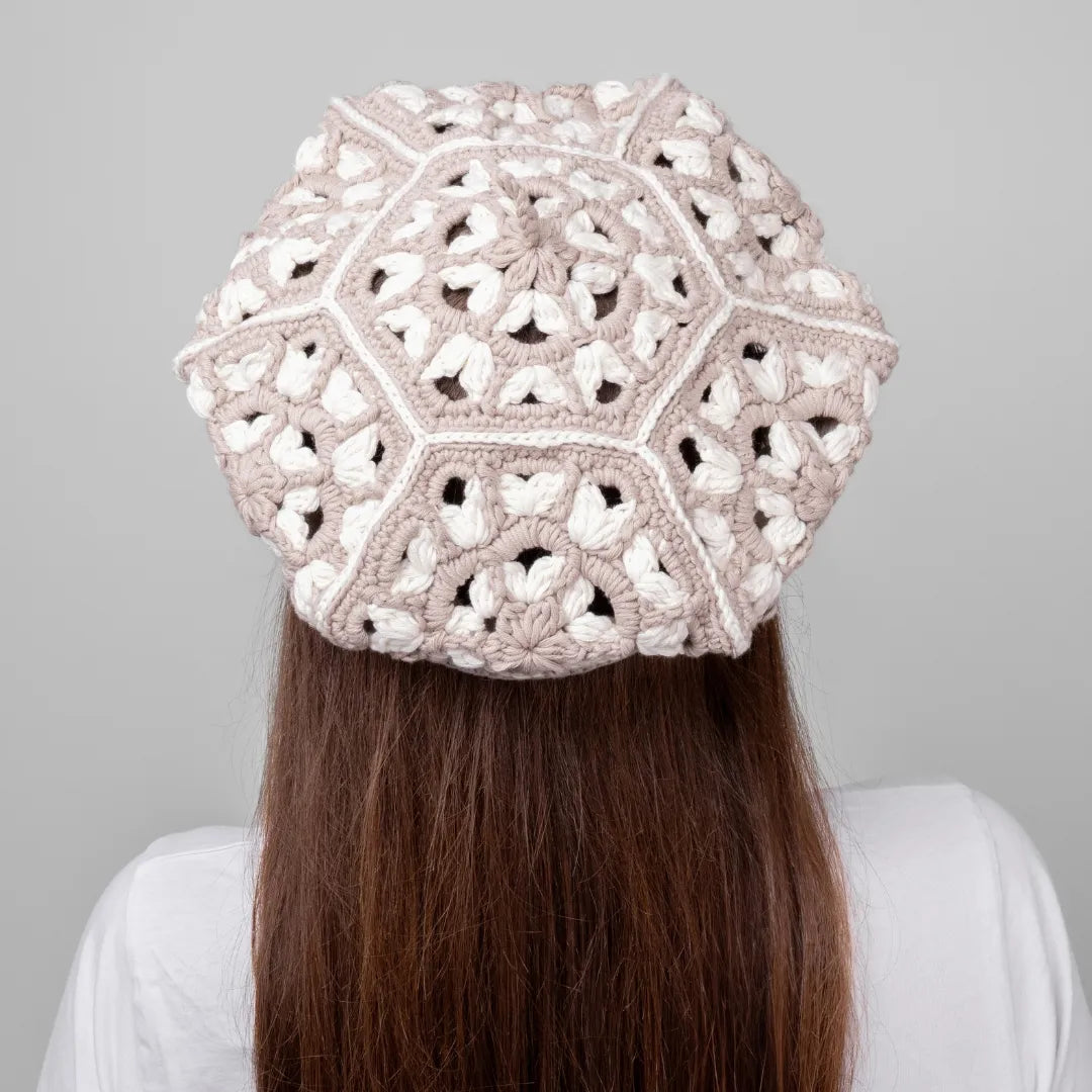 Person wearing a beige crochet hat against a gray background