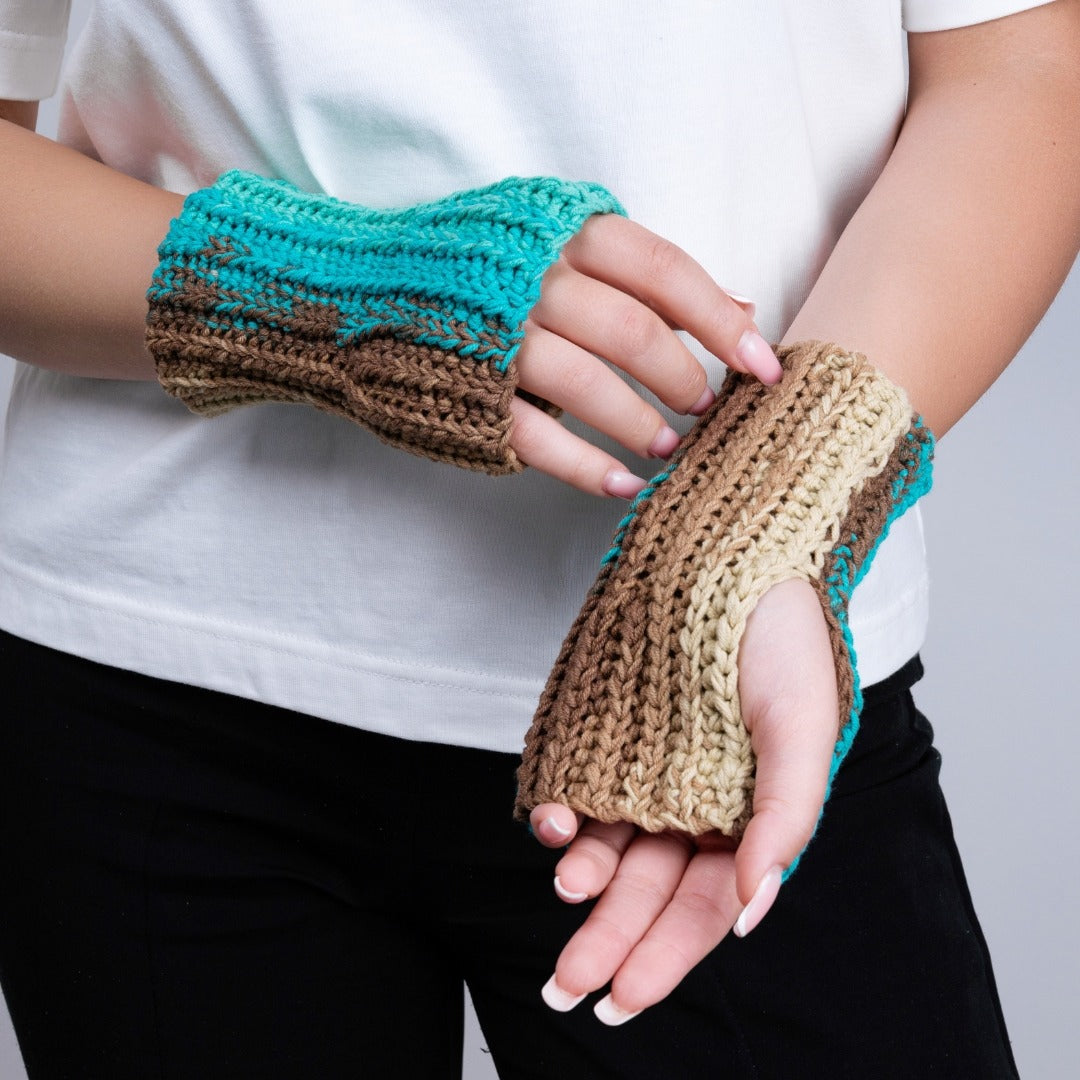 Person wearing turquoise and brown crocheted fingerless gloves against a plain background