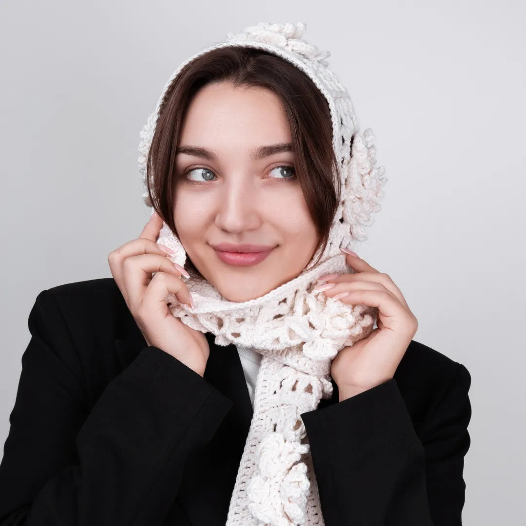 Woman wearing a white crocheted headscarf and scarf against a gray background